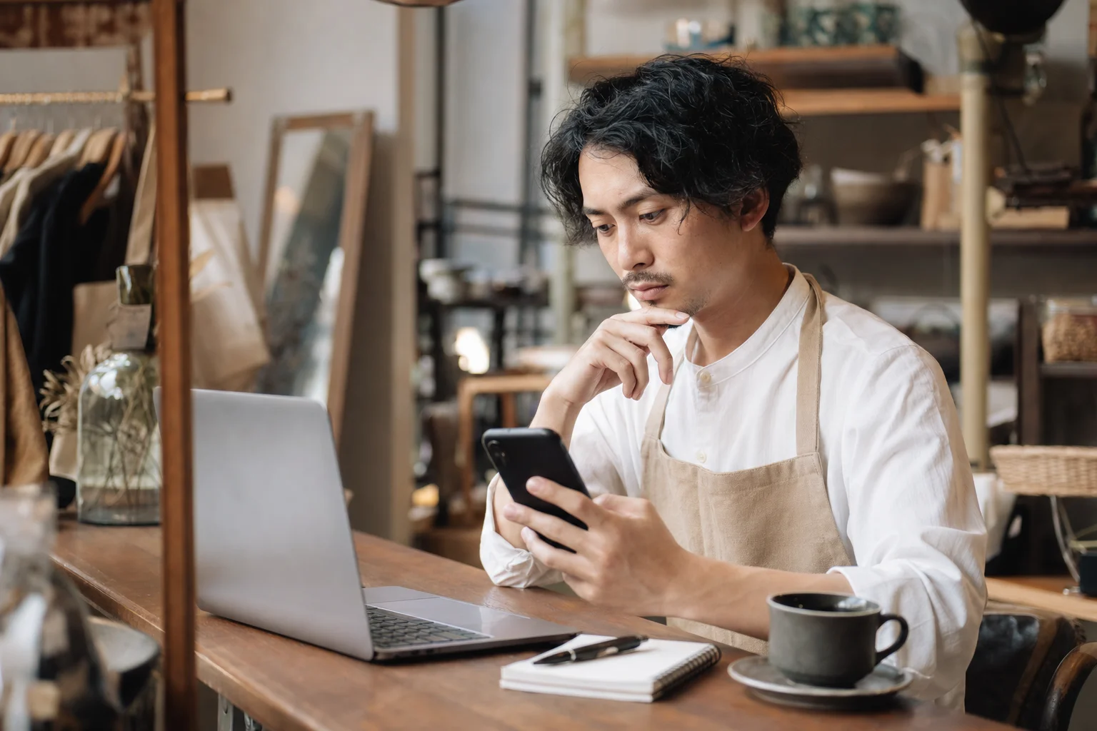 パソコンとスマートフォンを見比べながら集客方法を検討する店舗オーナー